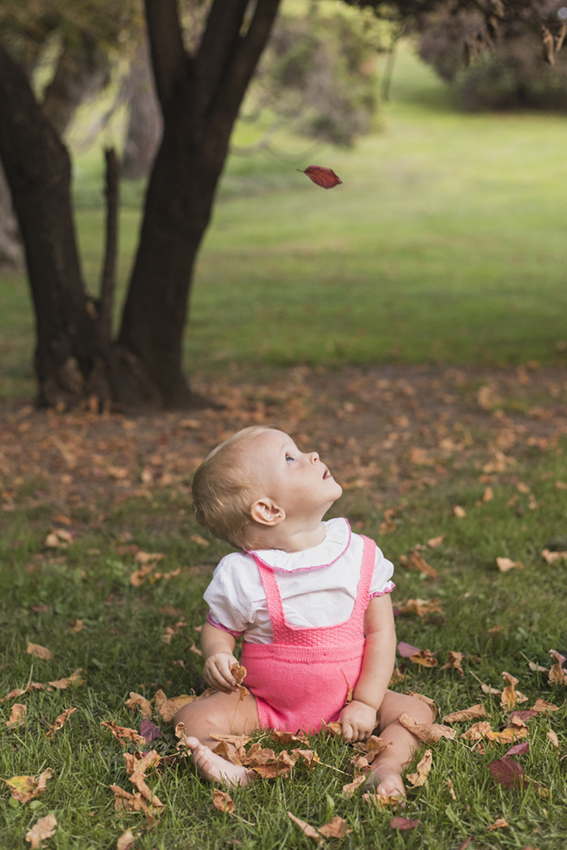Bebé sentada en jardin mirando a una hoja arriba de Momem Fotohgrafia