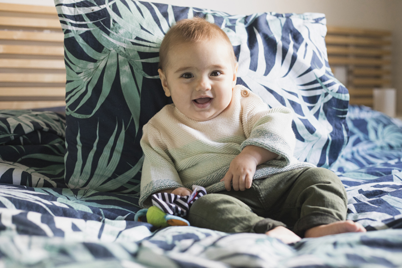 niño sentado en la cama riendo de Momem Fotografia